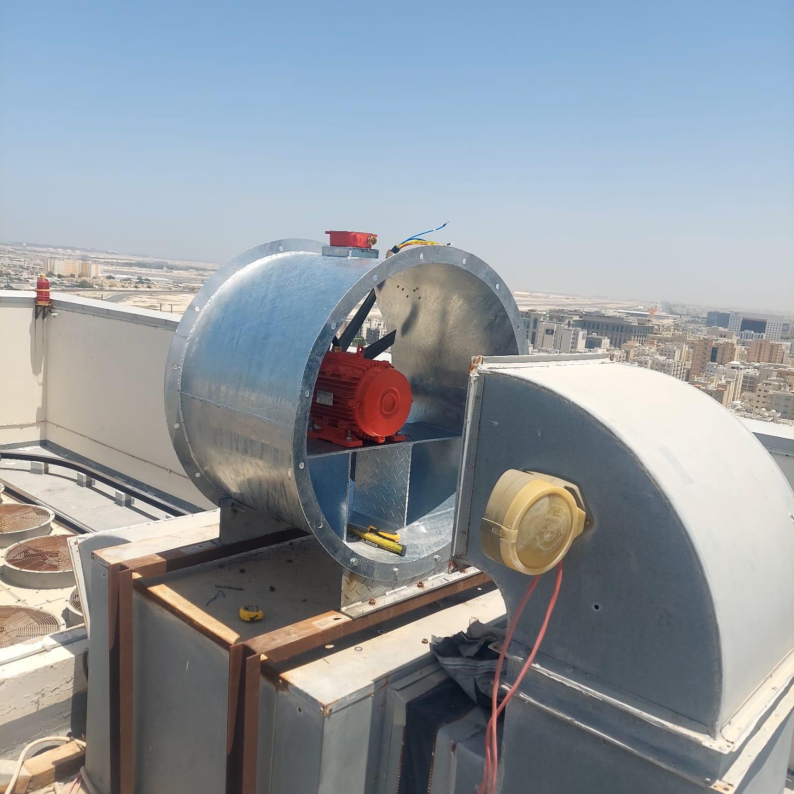 A galvanized rooftop ventilation fan with red motor, installed against the city skyline.