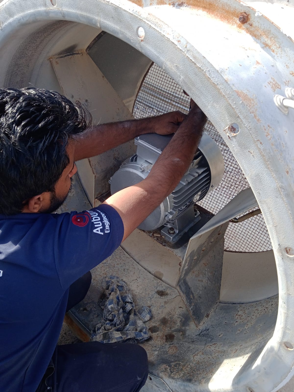 Servicing an axial fan motor behind its mesh guard — maintenance in action.